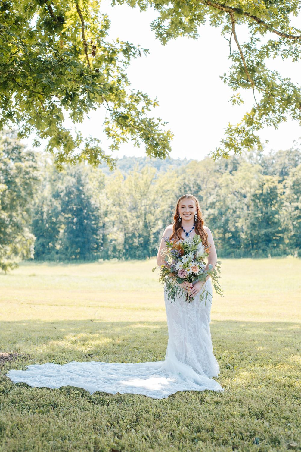 A beautiful bridal portrait in a sunlit field with a white lace gown and floral bouquet.