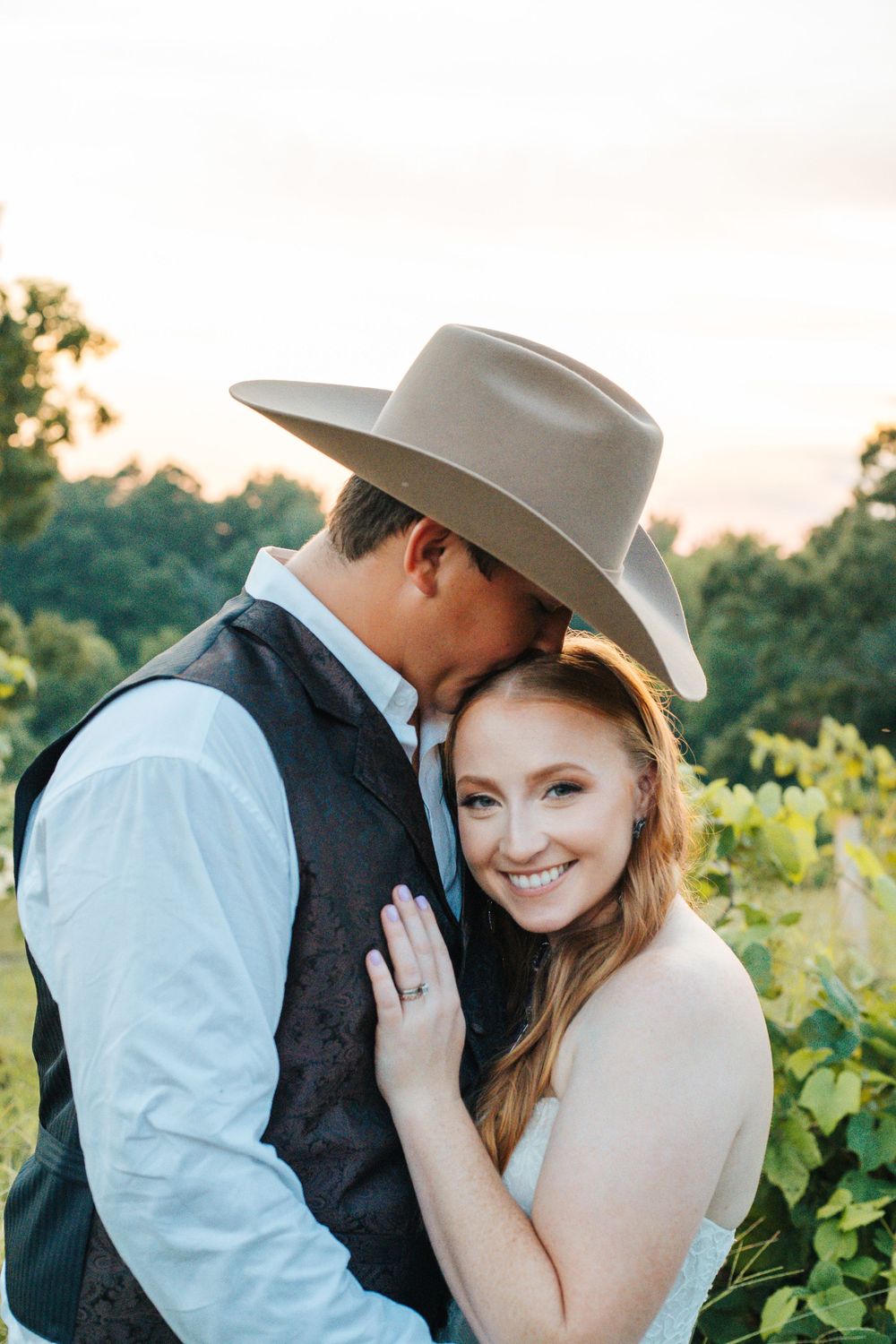 A romantic country wedding photo of a couple embracing in a vineyard at sunset.