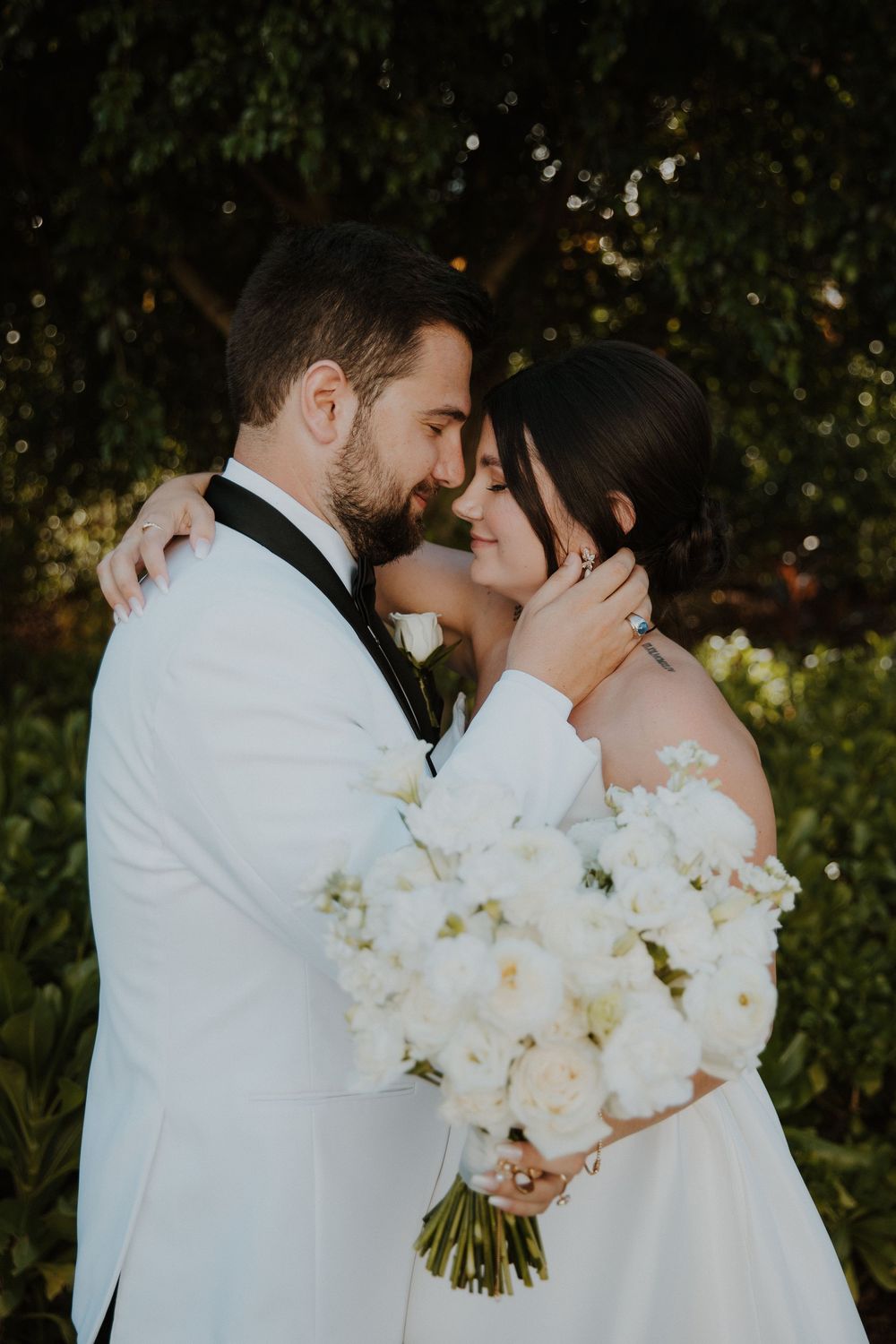 A romantic wedding moment captured in a garden setting with white floral bouquets and elegant formal attire.