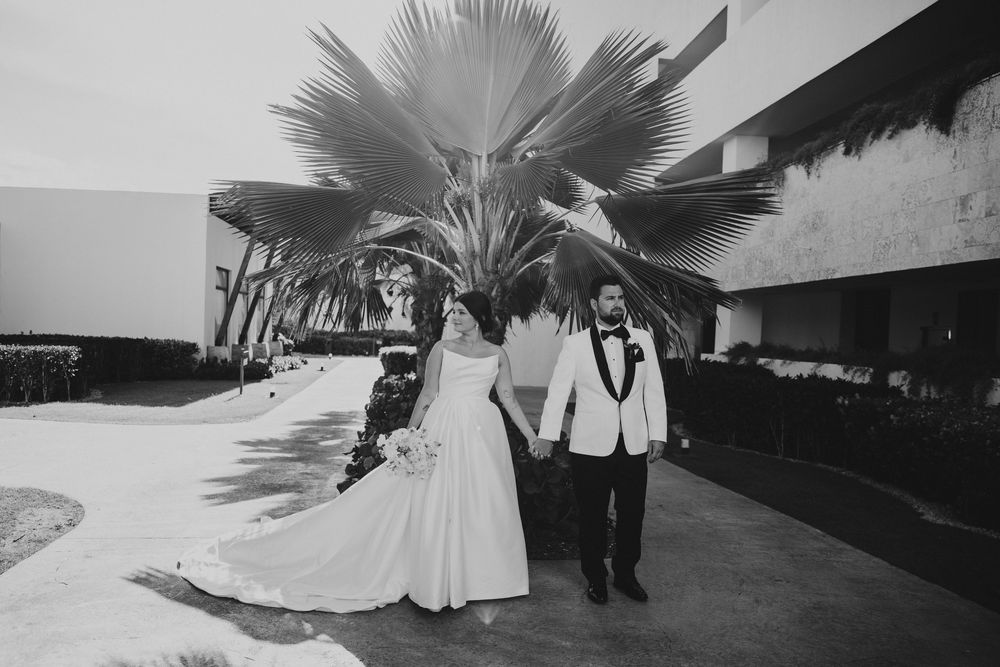 A couple walks along a path with a large palm tree overhead in a black and white wedding photo.