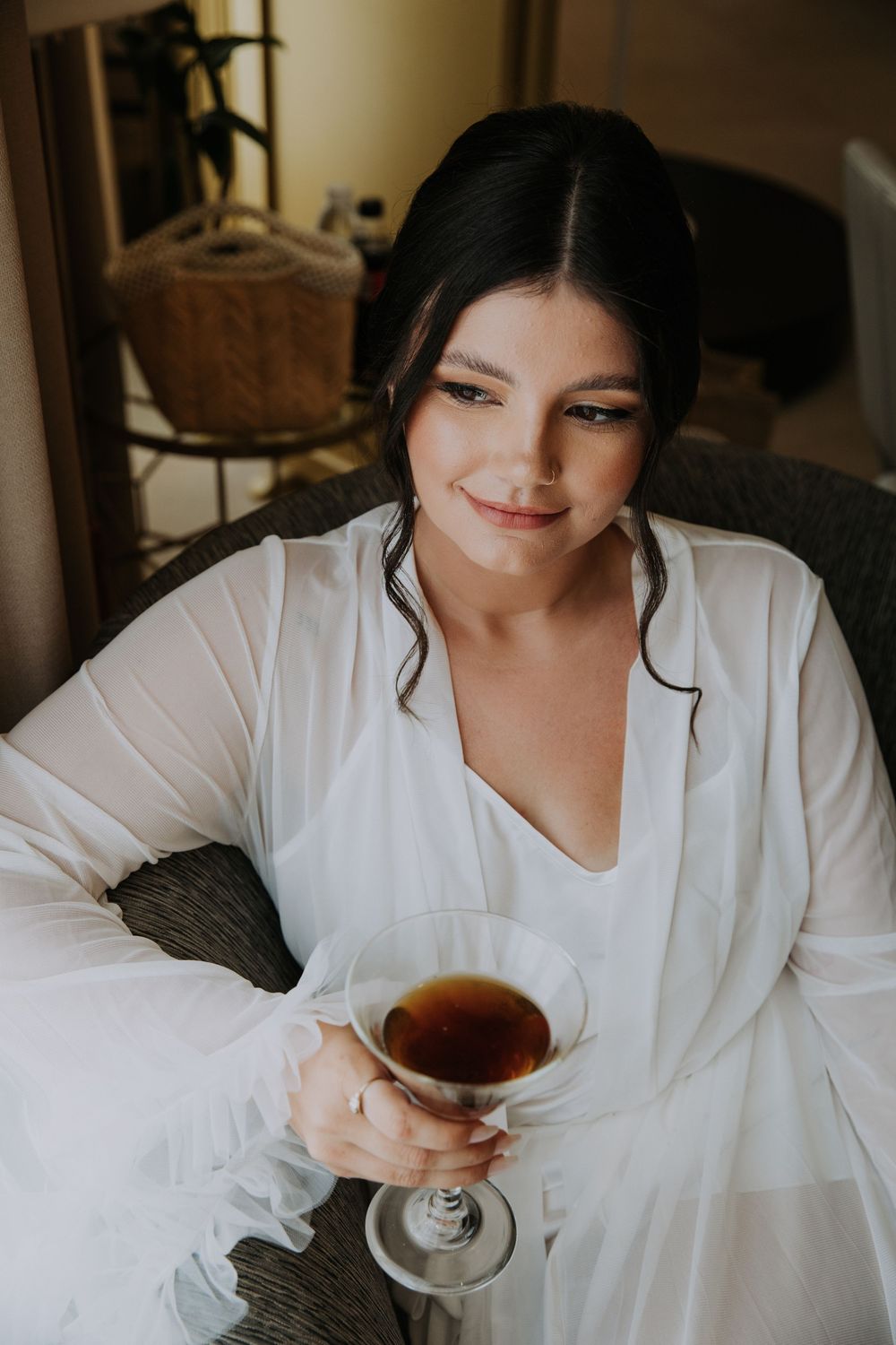 Woman relaxing in white robe while drinking tea in moody natural light.
