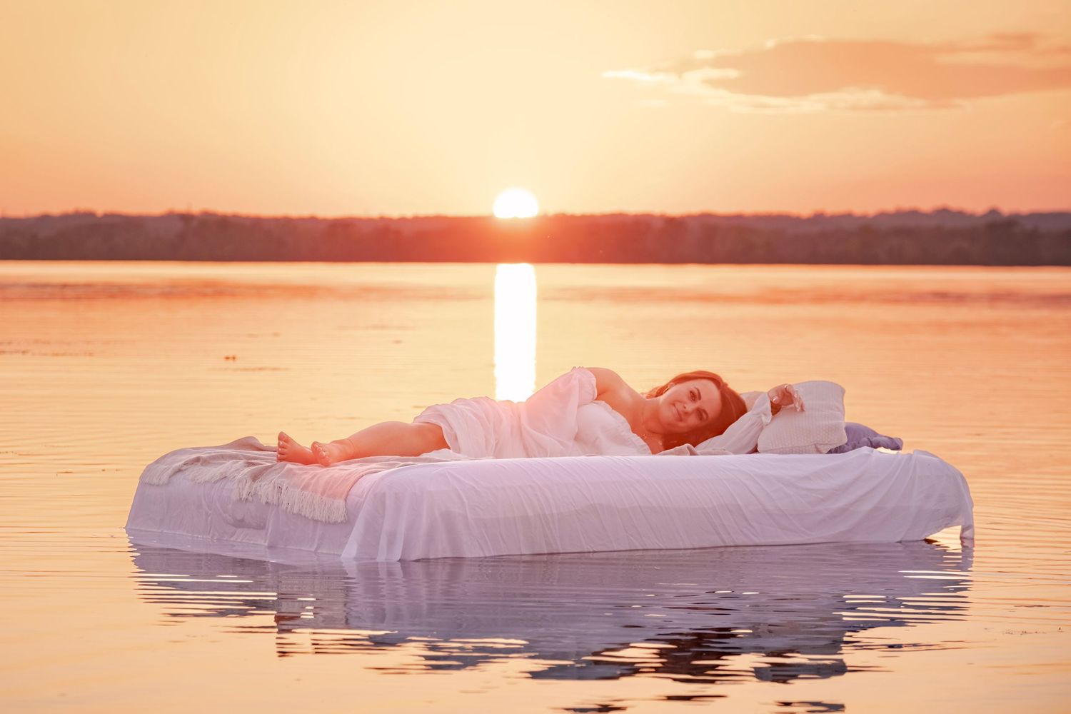 Scenic sunset over a tranquil lake with pink and orange sky reflecting on the calm water's surface.