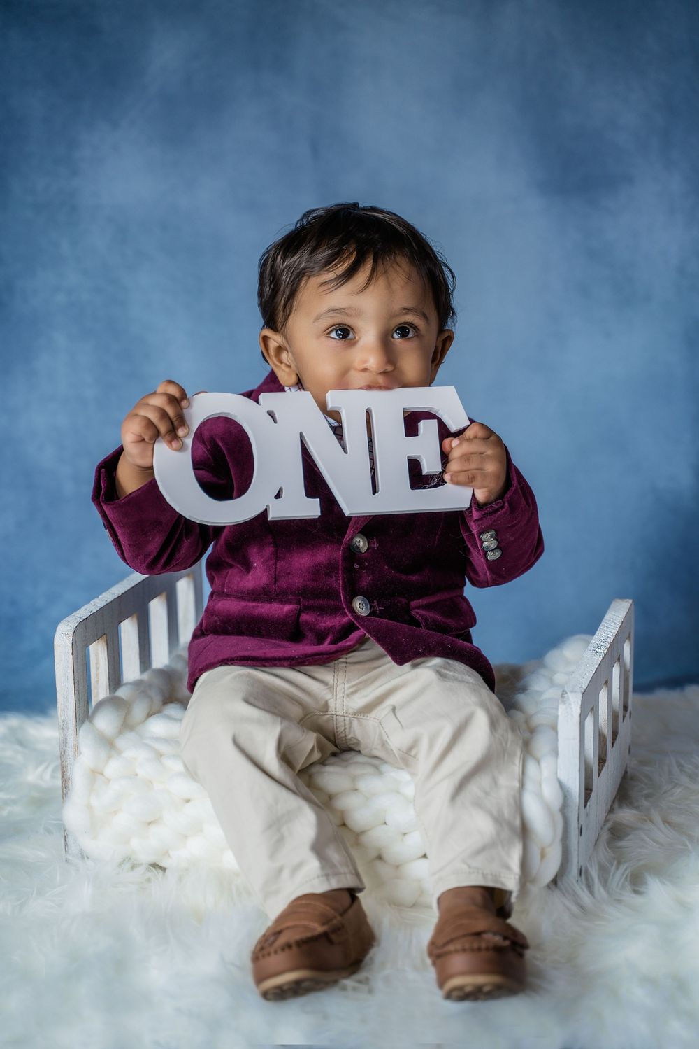 Professional studio photography series showing a small child on white chair against blue backdrop holding letter signs.