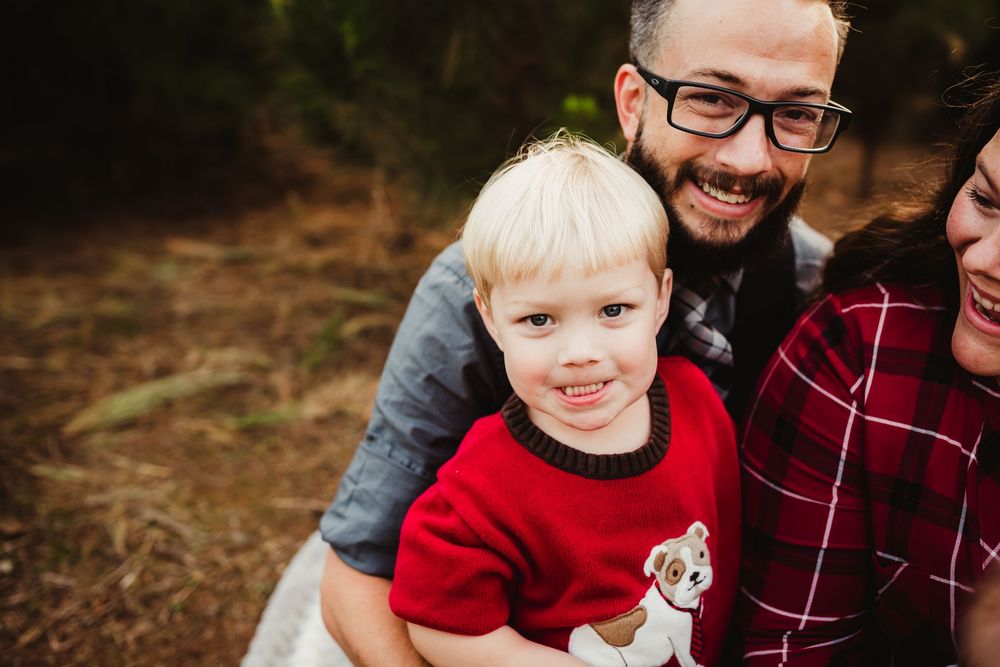 A playful family photo session captured in a wooded outdoor setting with red and burgundy clothing.
