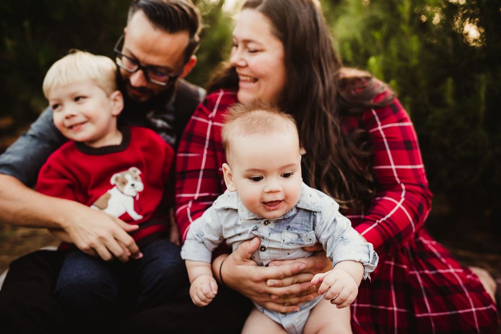 Family wearing coordinated red plaid outfits sitting outdoors during an autumn photography session.