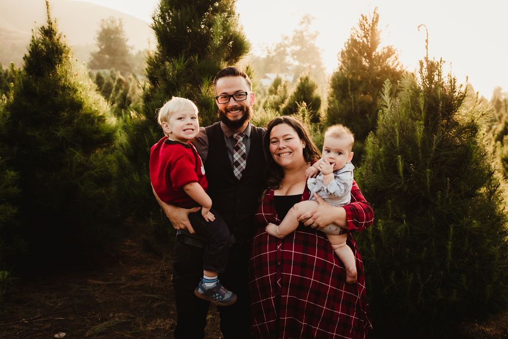 A family embraces outdoors during golden hour with evergreen trees in the background.