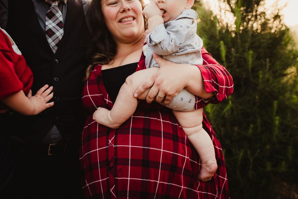 A person in a red plaid flannel shirt holds a baby outdoors during golden hour.