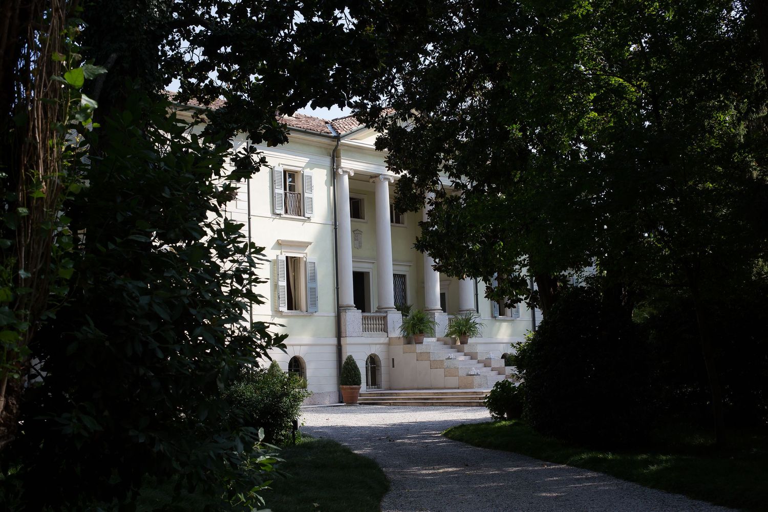 Tree-lined pathway leading to a white neoclassical building with columned portico.