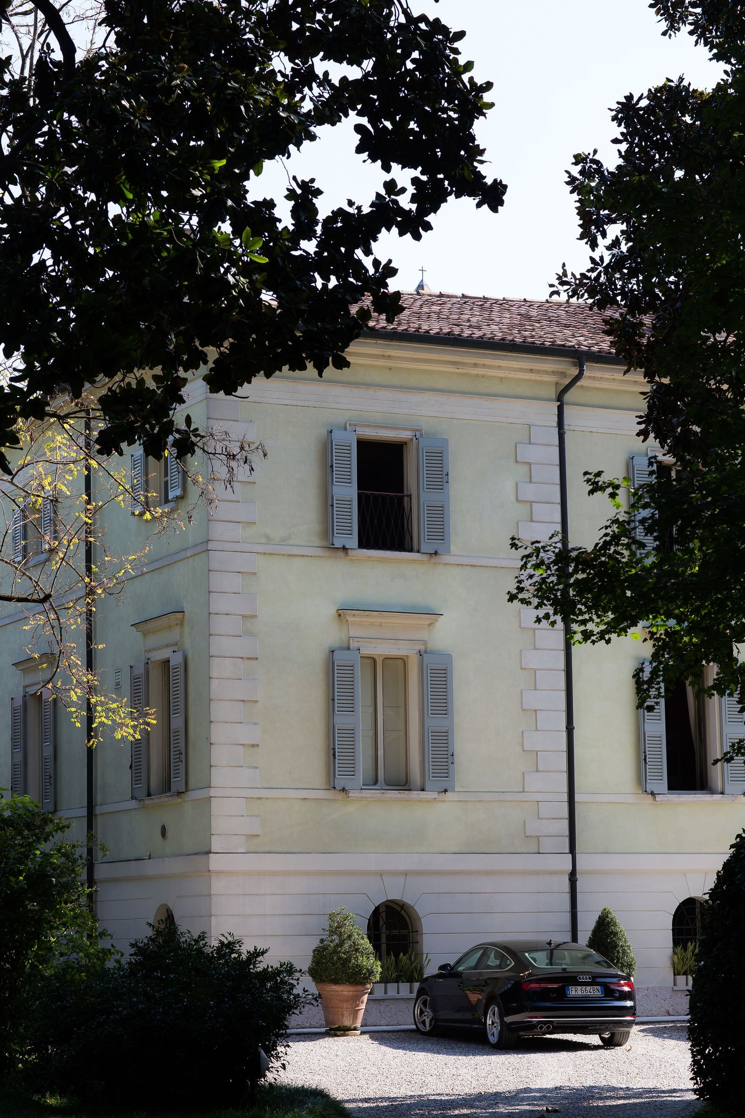 Exterior view of an elegant cream-colored villa with white trim and gray shutters.