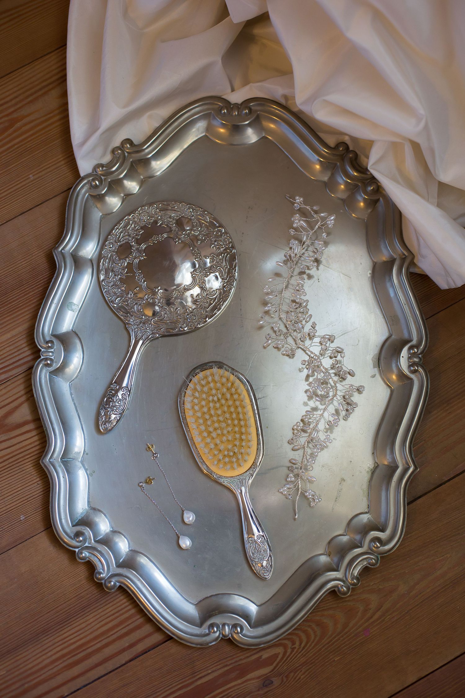 Vintage silver vanity tray with ornate designs and decorative brushes on wooden surface.