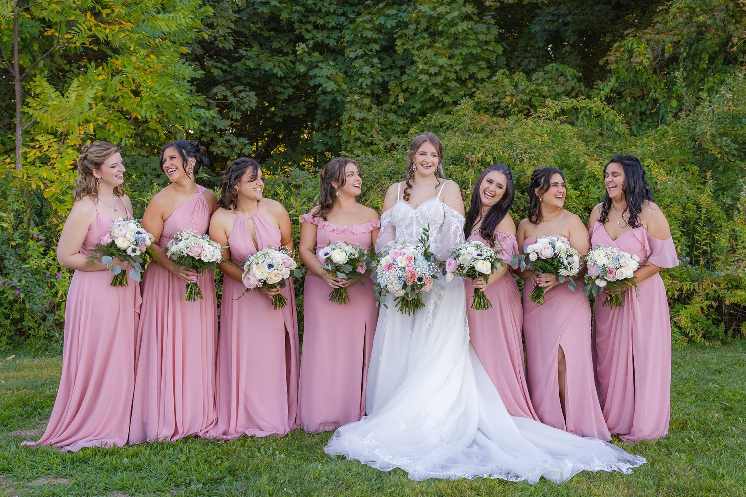 A bridal party in pink dresses poses outdoors at a garden wedding venue.