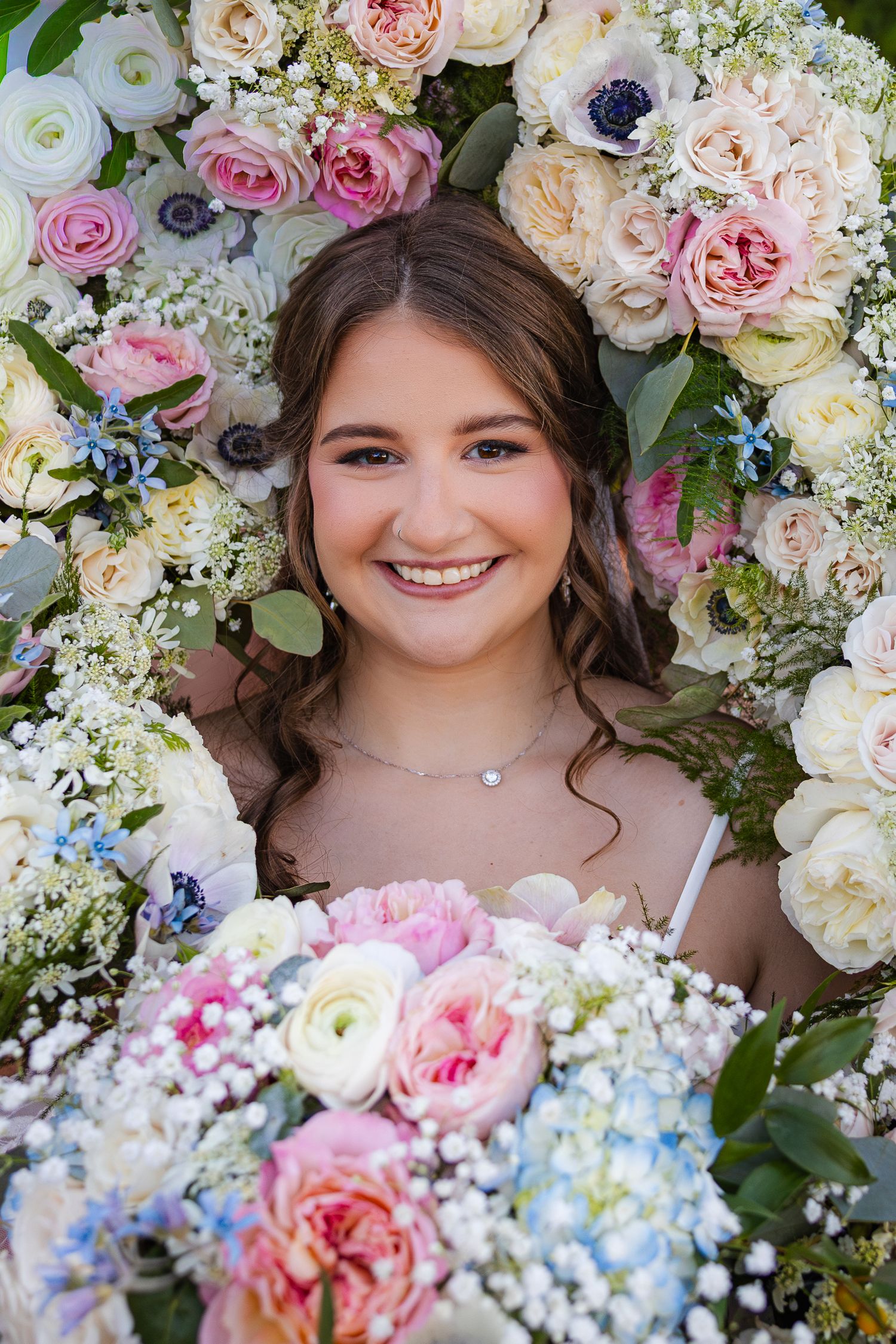 Wedding bouquet arrangement features pink roses, white ranunculus and blue delphinium with greenery.