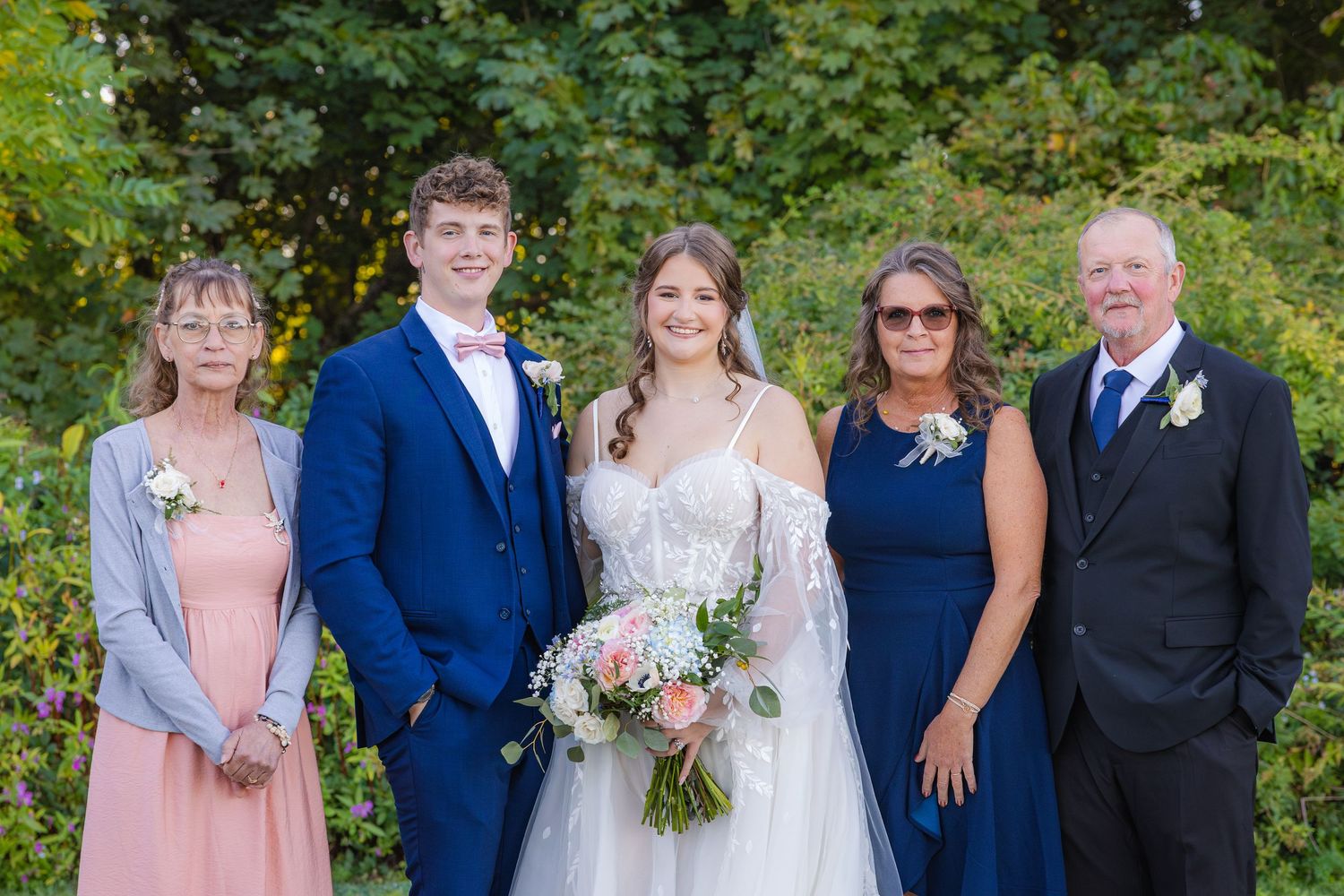 A wedding party poses together outdoors wearing coordinating blue and pink attire for formal group photos.
