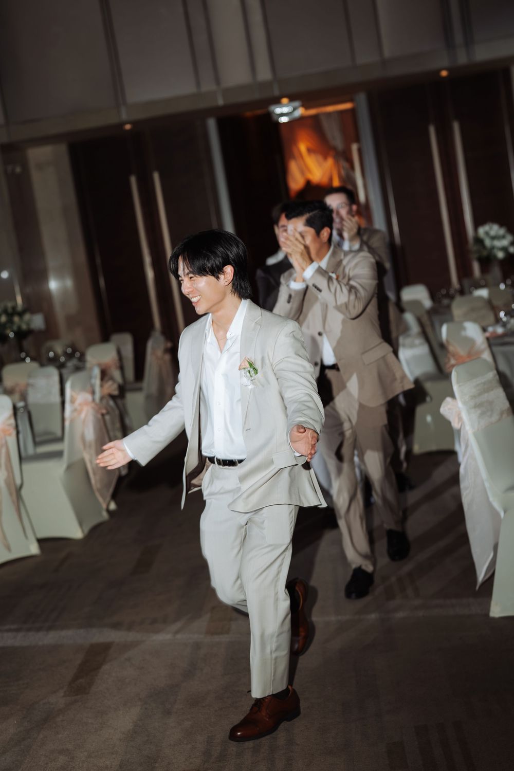 Smiling groom in ivory suit making grand entrance at wedding reception venue.