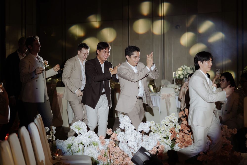 Wedding party guests celebrating on stage with flowers at elegant reception venue.