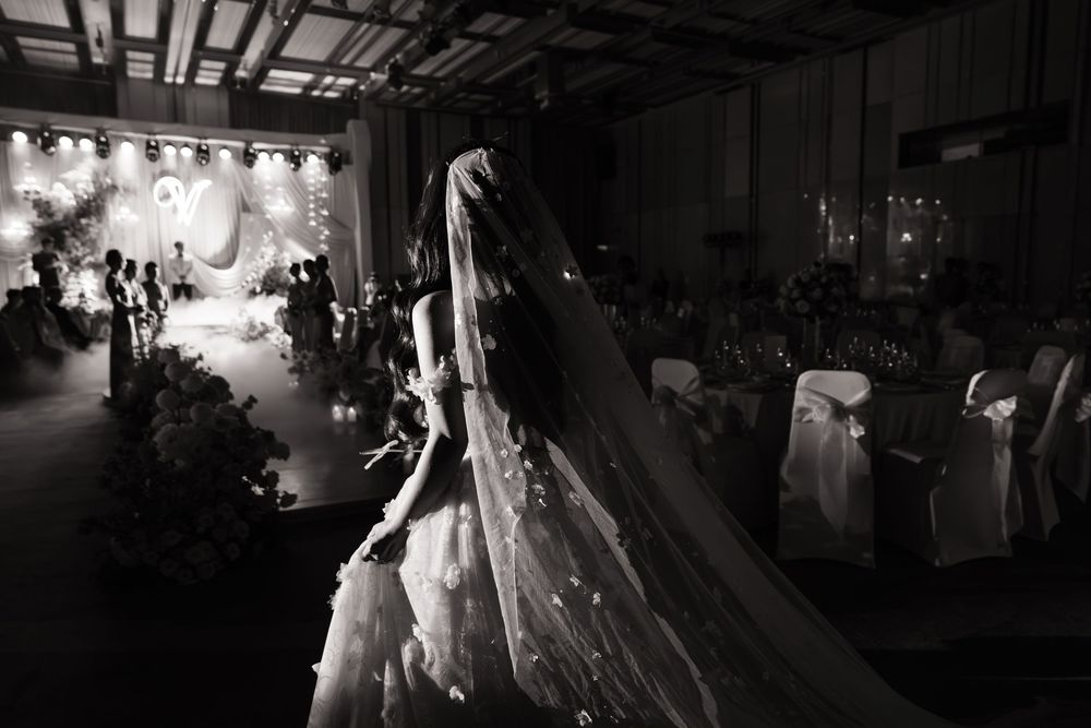 Black and white photo of a bride in a flowing gown and veil walking down a decorated wedding aisle.