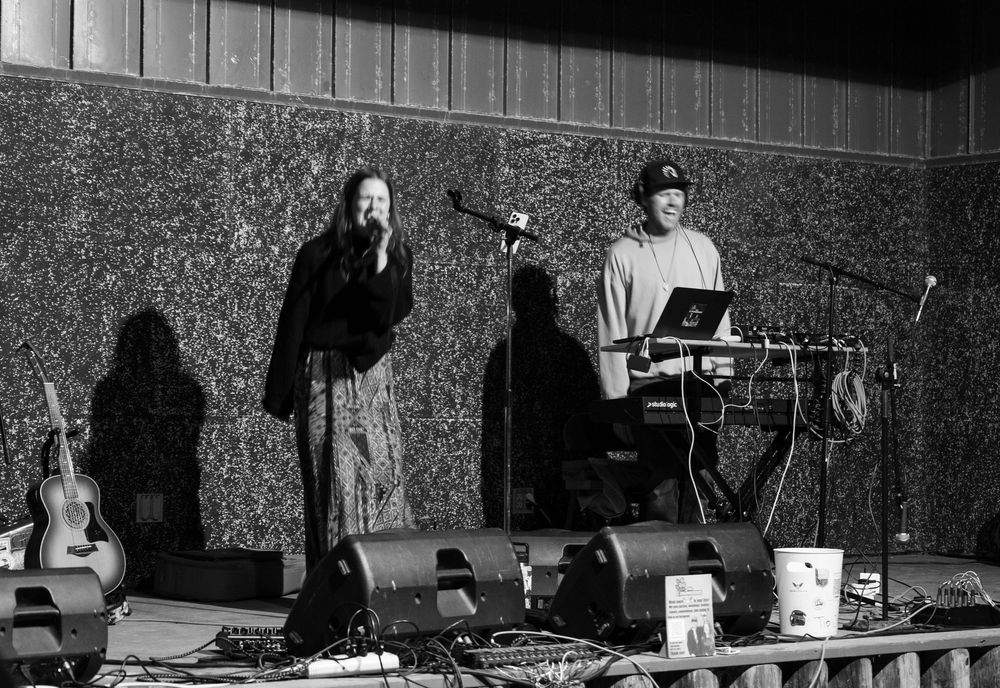 Musicians performing on stage with electronic equipment and acoustic instruments in monochrome.