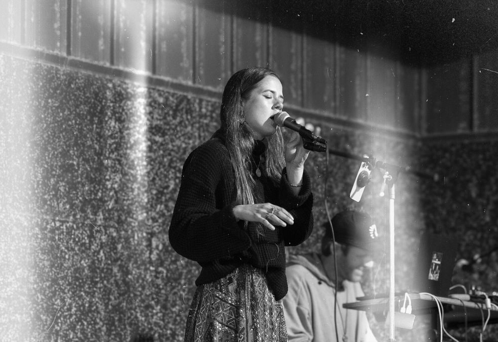 Performer silhouetted on stage singing into a microphone during a dark atmospheric concert performance.