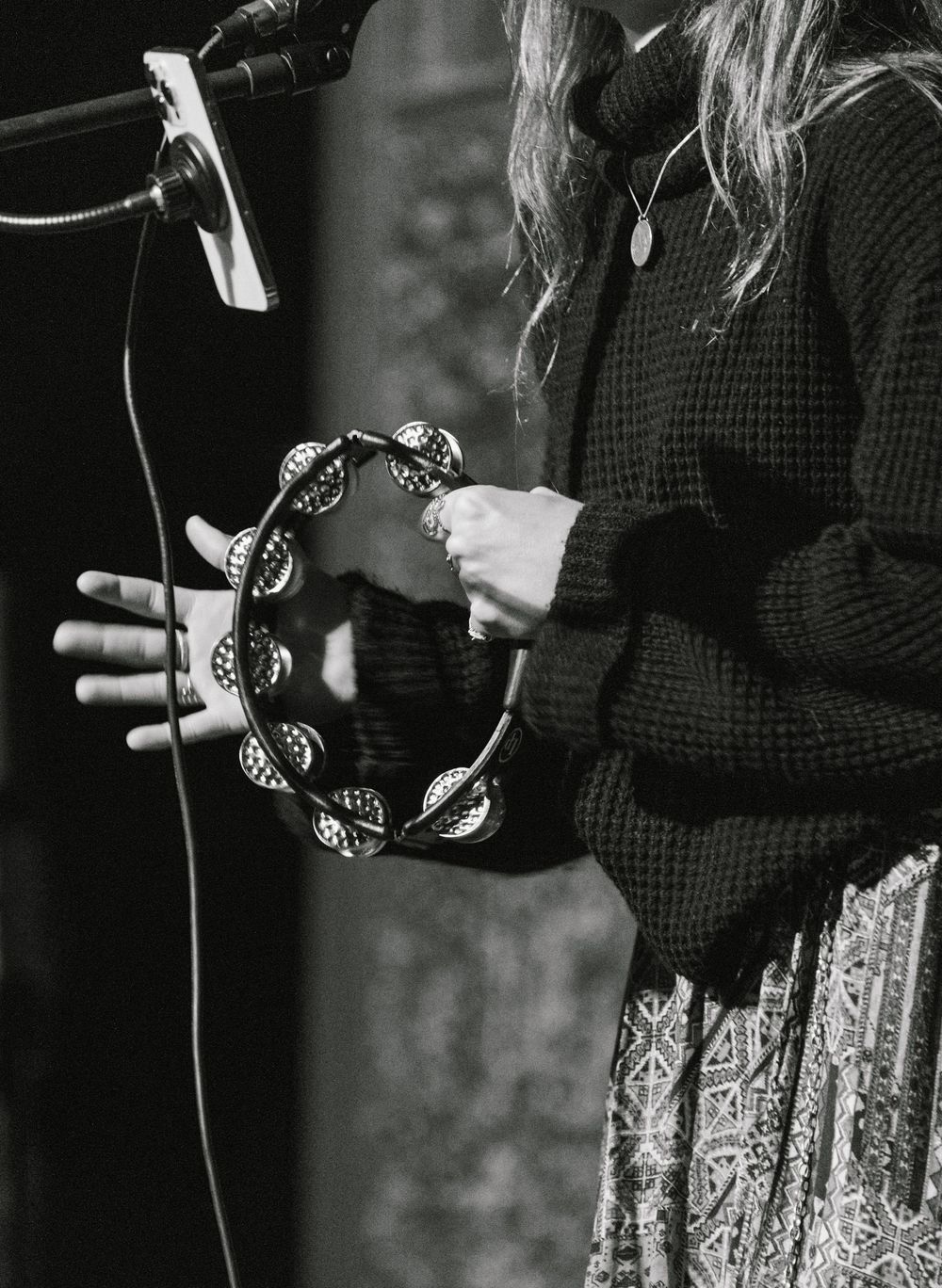 Close-up black and white image of hands holding a decorated tambourine near a microphone.