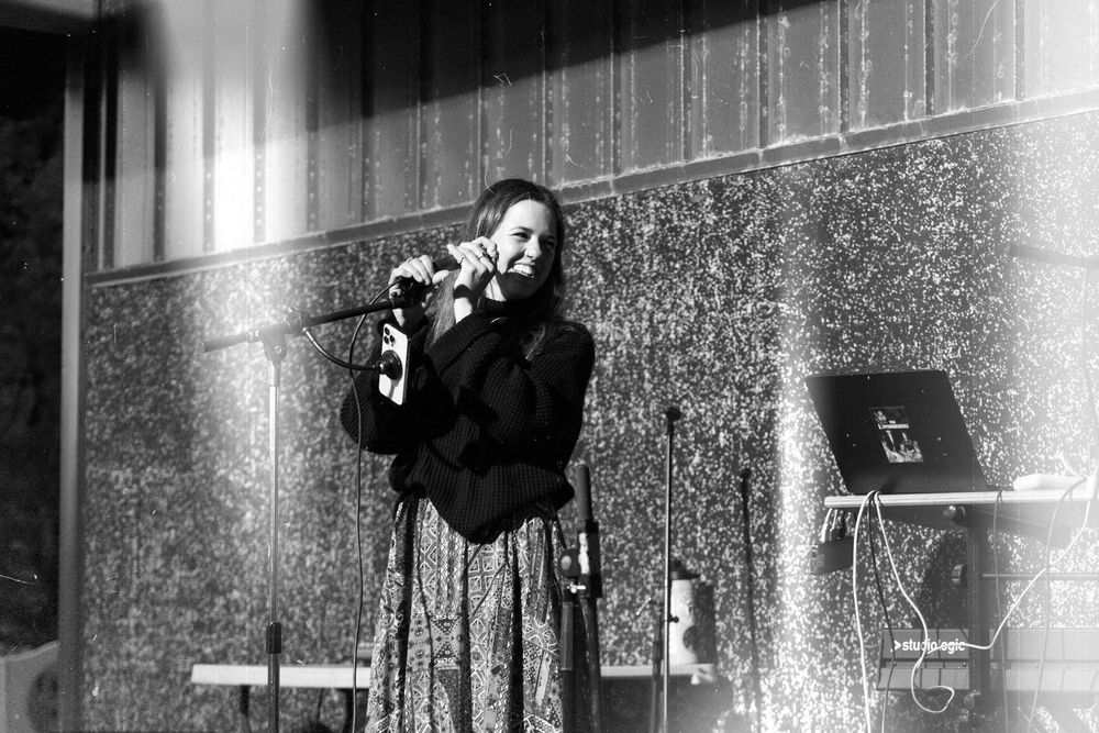 Black and white photo of a performer singing on stage in front of a textured wall.
