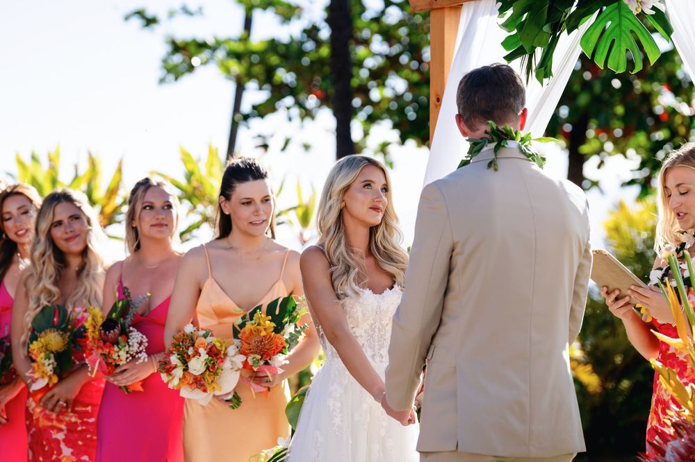 Wedding party laughs together under tree canopy during outdoor summer celebration.
