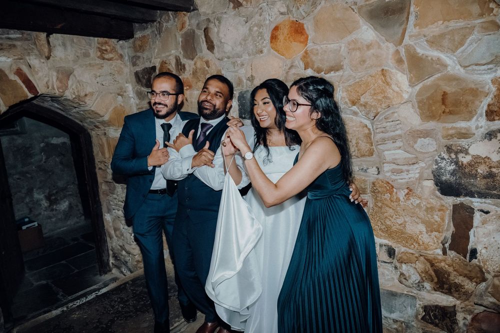 Happy guests in formal attire dance during a festive celebration in a rustic stone building.