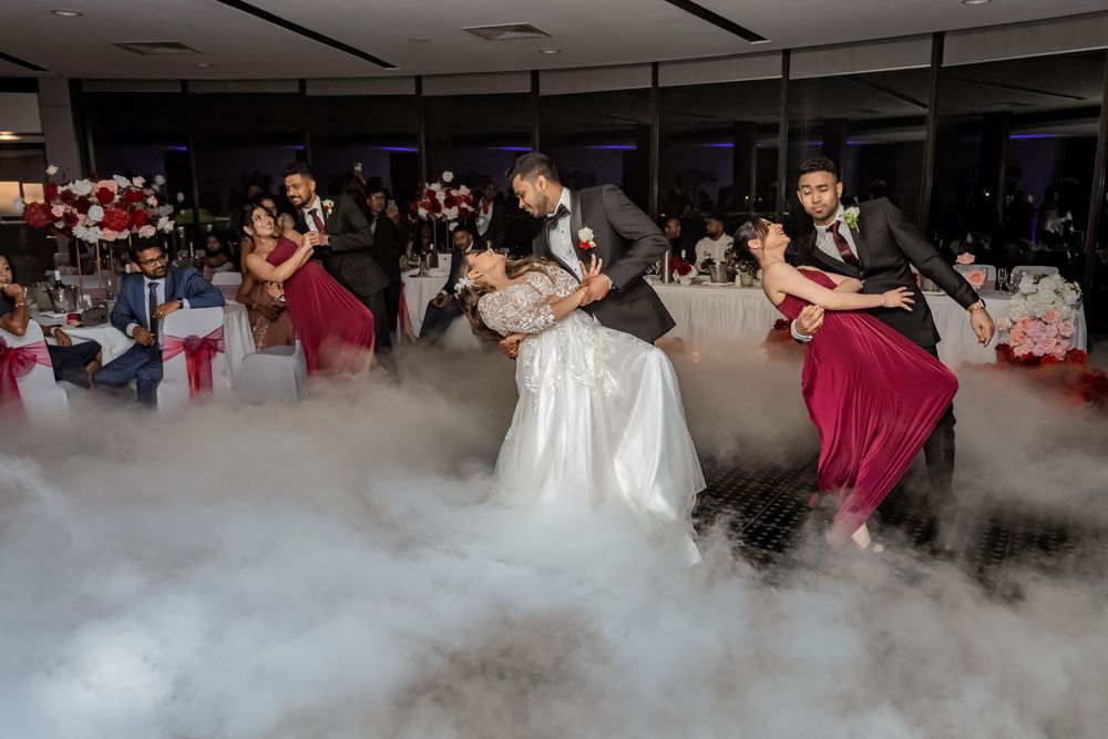 Wedding guests dancing in a reception hall with dramatic white fog effects on the dance floor.