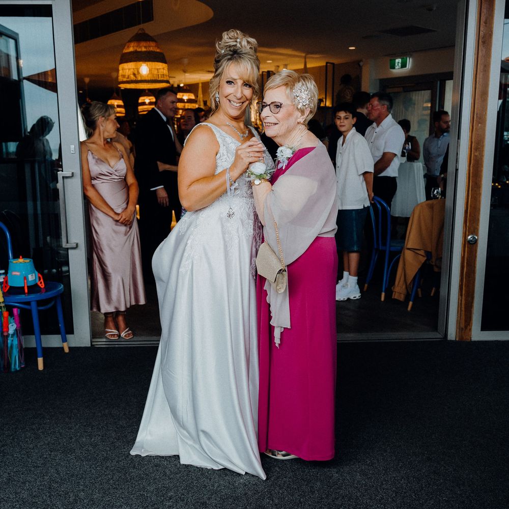 Wedding celebration moment shared between two elegant guests in white gown and fuchsia dress at indoor venue.