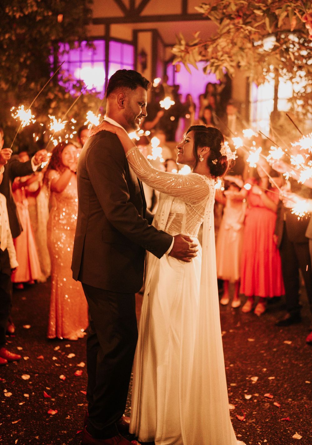 Newlywed couple dances surrounded by guests holding sparklers creating a magical nighttime glow at outdoor wedding reception.