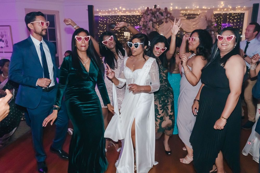 People dancing and celebrating at a lively wedding reception with sparkling lights in the background.
