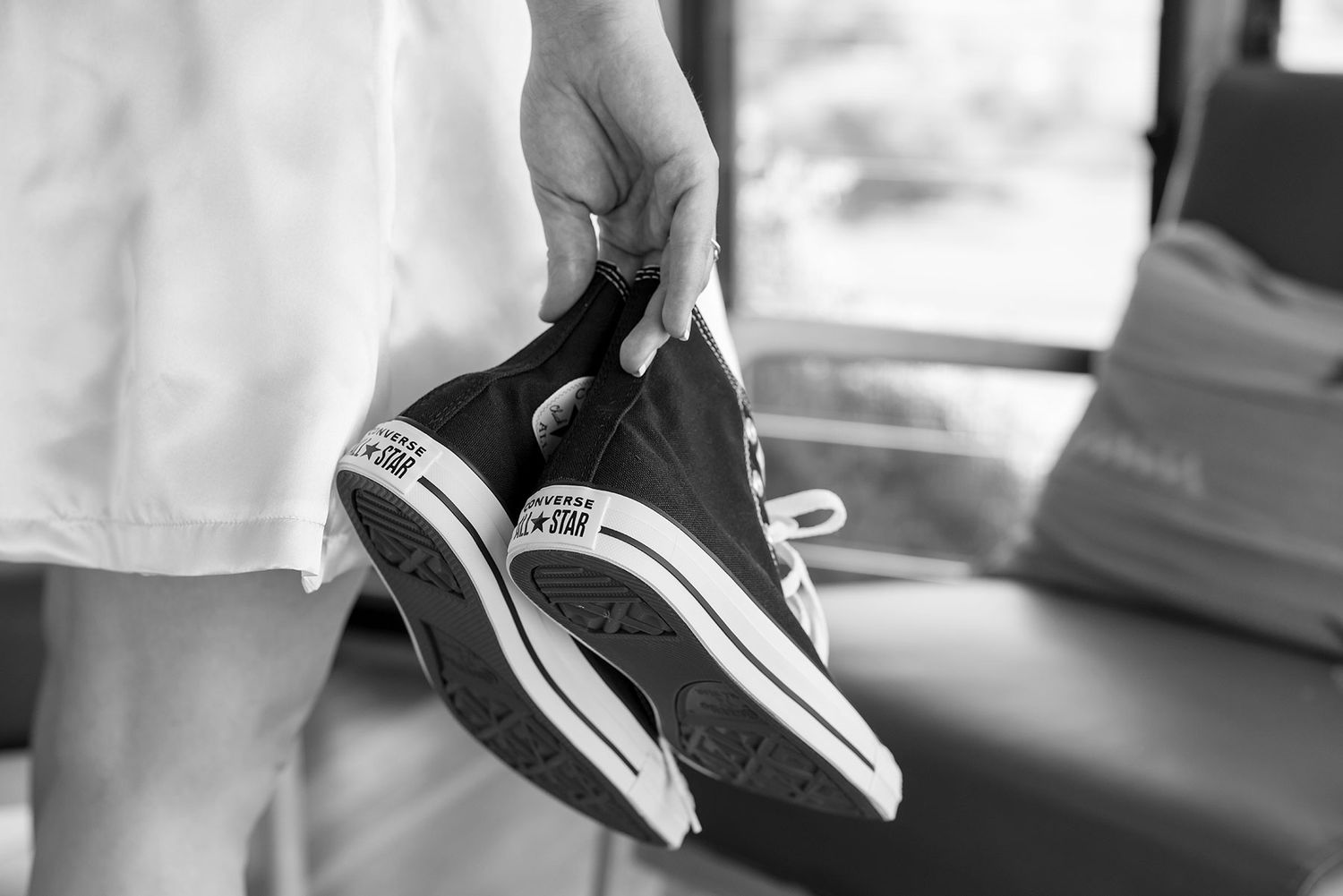 A close up black and white image of a brides hands holding her black Converse All Star wedding shoes