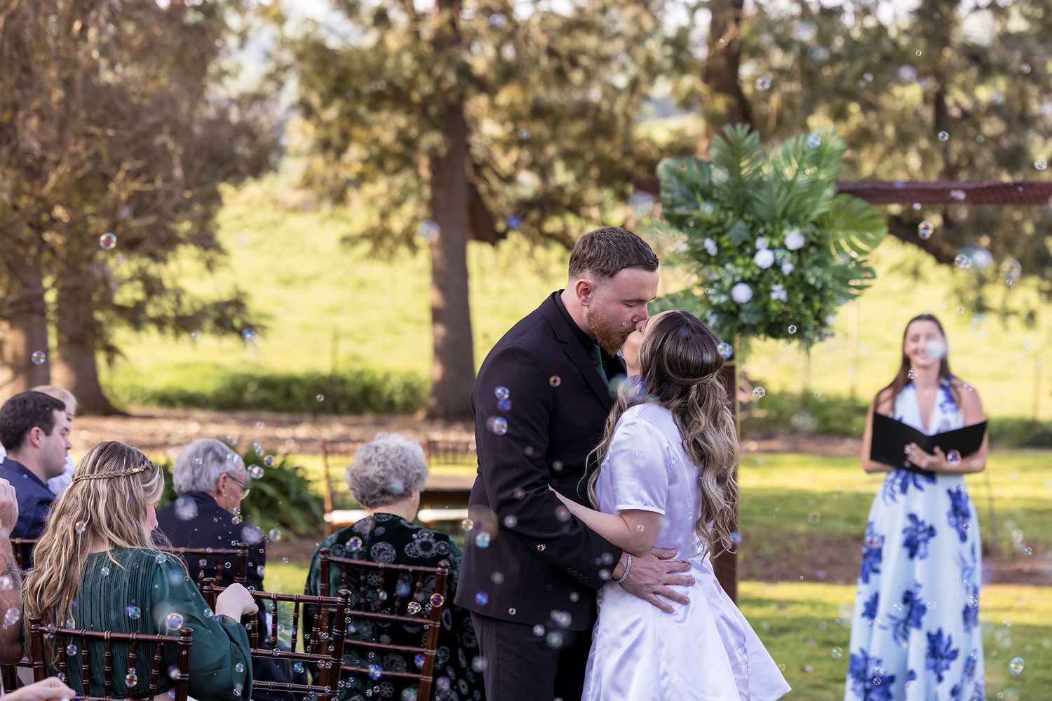 A Bride and Groom share a kiss together during their outdoor wedding ceremony with bubbles floating around them at Kimo Estate.