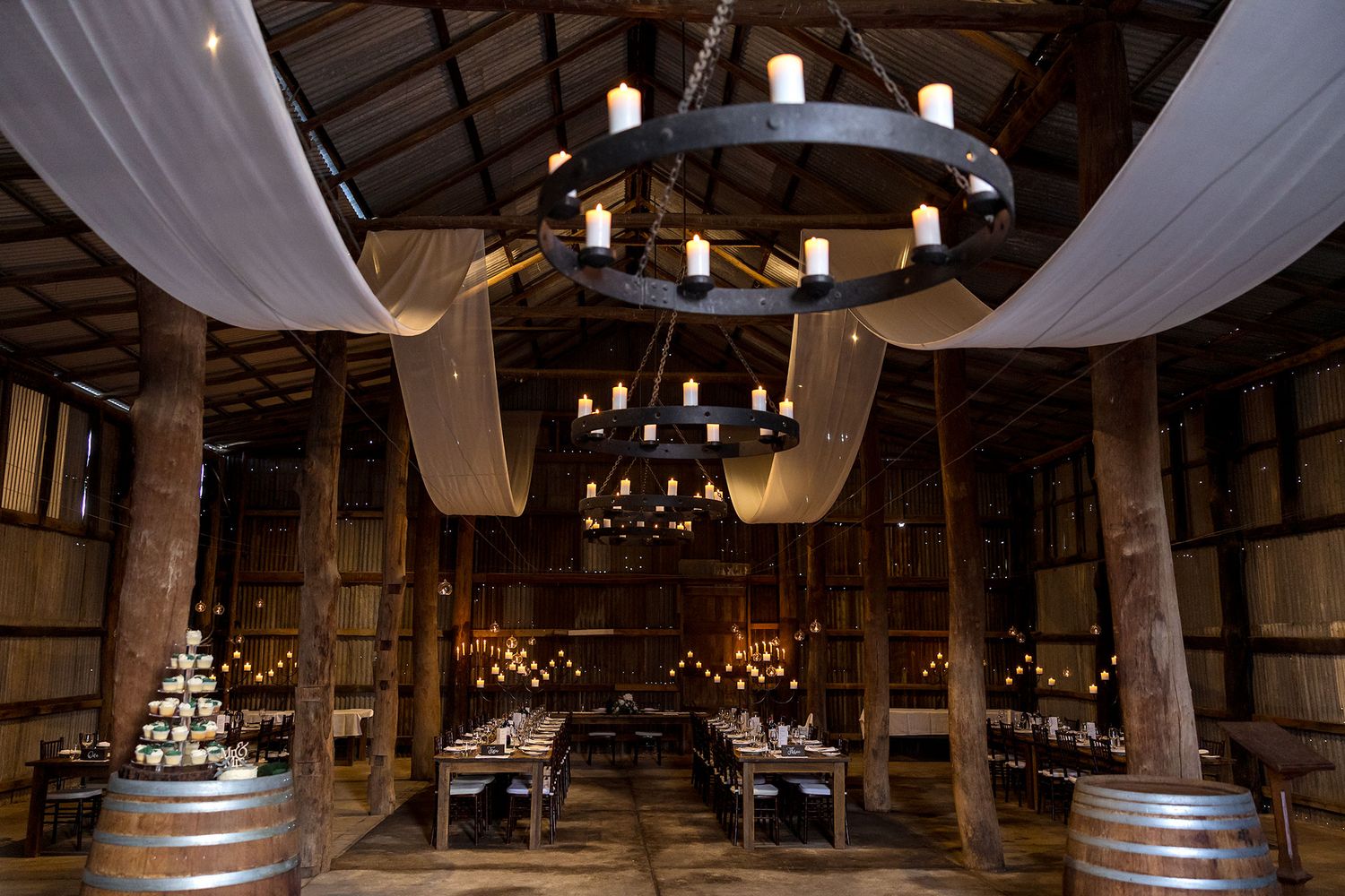 Interior view of a rustic barn wedding venue with exposed wooden beams and romantic string lighting throughout at Kimo Estate.