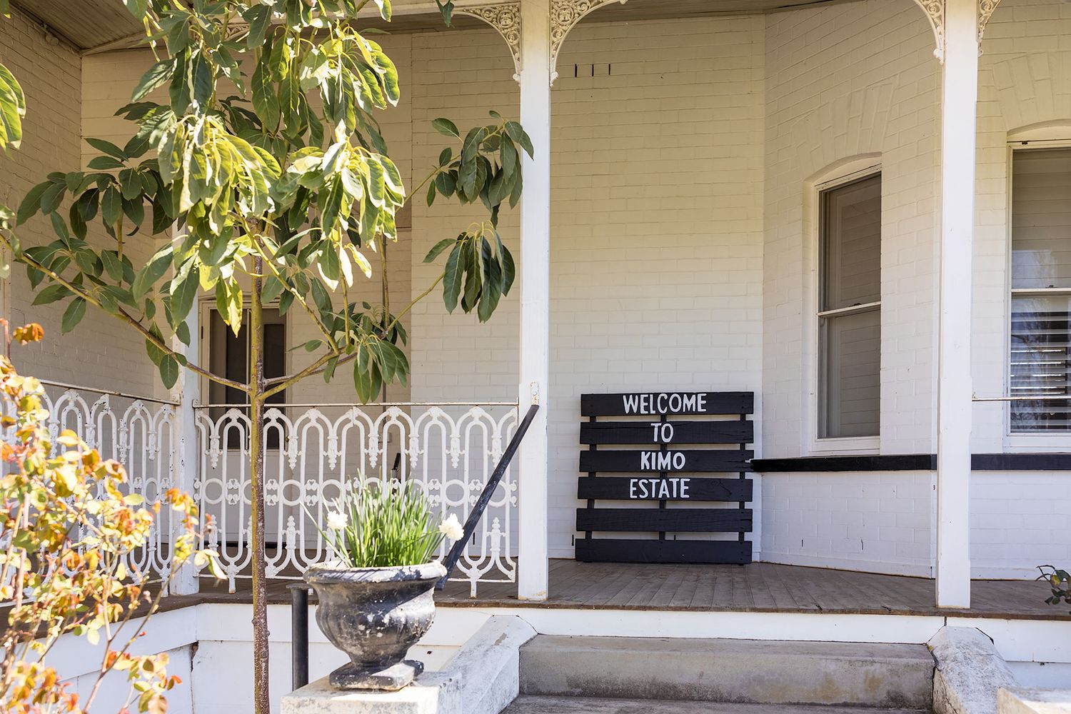 A serene covered porch with white columns and black benches wraps around a colonial-style building with tropical foliage at Kimo Estate.