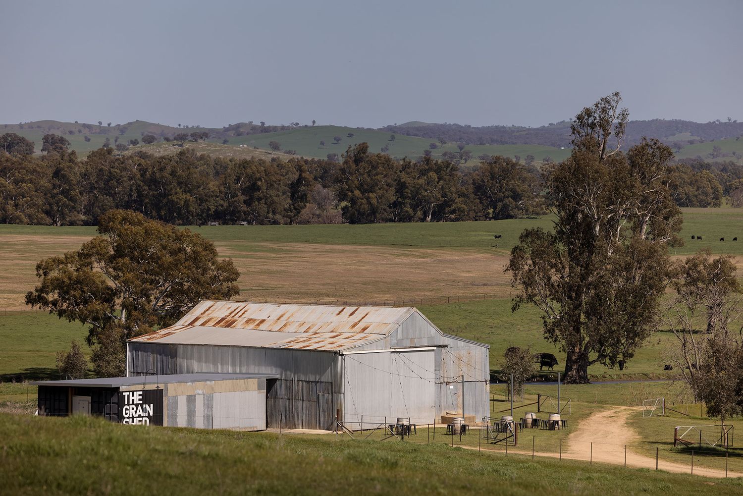 Rural landscape with metal farm buildings and eucalyptus trees scattered across rolling hills in the Australian countryside at Kimo Estate.
