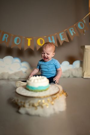A first birthday cake smash photo series showing a baby in blue exploring and smashing a turquoise and white frosted cake.