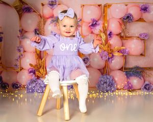 A one year old baby sits surrounded by pink floral decorations at a birthday celebration with glowing candles and sparklers.