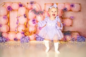 Glowing marquee letters decorated with purple flowers create magical first birthday photo scene.