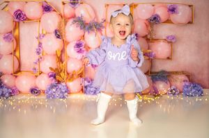 A festive scene with pink and purple balloons, twinkle lights, and decorative birthday party setup against a rosy backdrop.