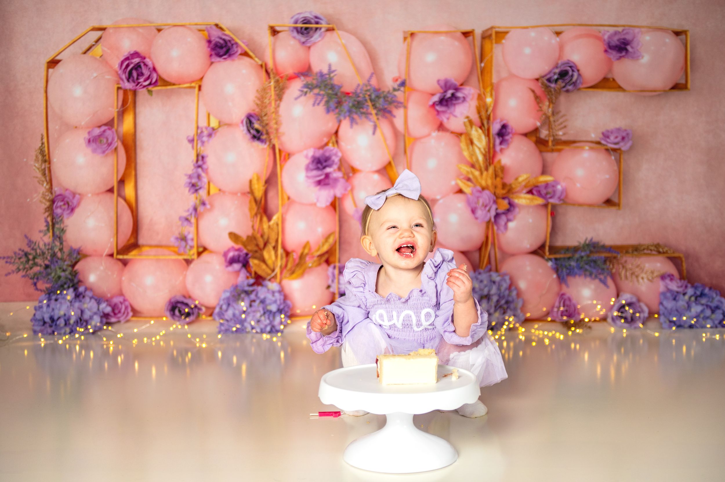 Beautiful wedding dessert table setup with a white cake decorated with pink and purple floral arrangements.