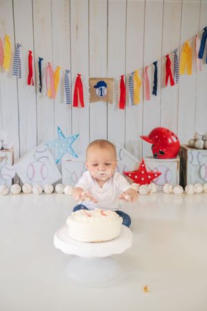 Festive first birthday party scene with colorful bunting and white cake smash setup against wooden wall backdrop.