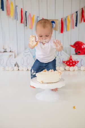 White cake smash photo session setup with colorful banner decorations and white wood floor backdrop for birthday celebrations.