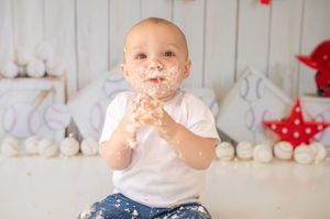 Happy baby stands next to polka dot banner at birthday party celebration with stuffed animals and red decor.