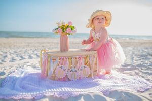 A series of beach portraits featuring a birthday celebration setup with pink accessories and floral decorations on white sand.