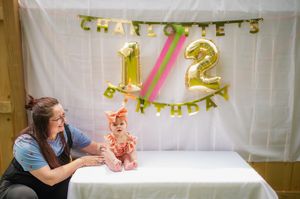A birthday celebration setup with gold number balloons 1/2 and a person at a table with pink decorations.