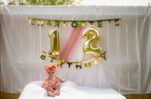 Half birthday party setup with gold number balloons reading '1/2' against a white backdrop and party decorations.