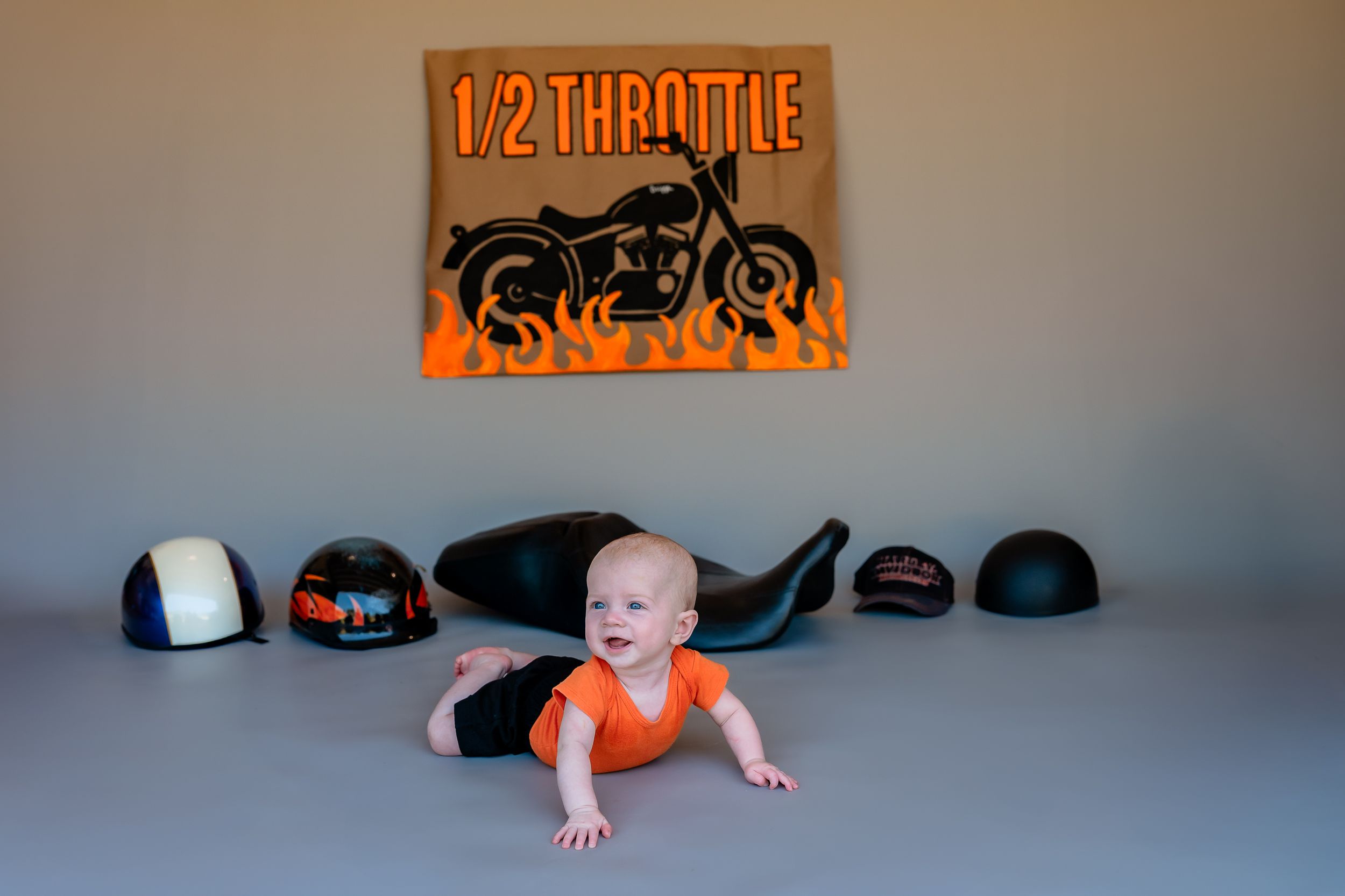 Baby in orange onesie performs the army crawl position across a gray floored room.