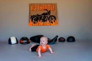 Baby in orange onesie performs the army crawl position across a gray floored room.