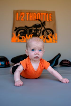 Baby in orange onesie lying on gray surface does army crawl motion in sequential photo series.