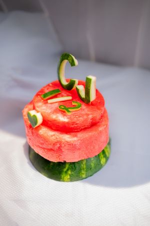 A watermelon slice topped with decorative cucumber curls arranged artistically on a white surface.